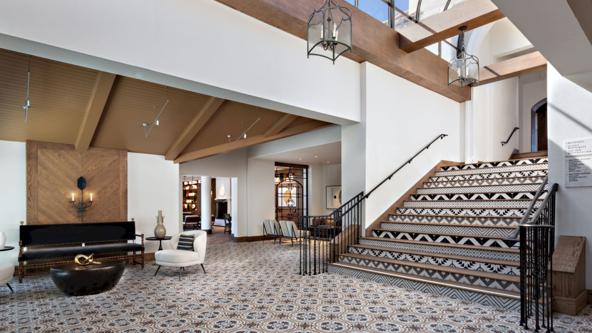 Spacious, modern interior with patterned floor and staircase, cozy seating, decorative lamps, and wooden ceiling beams.