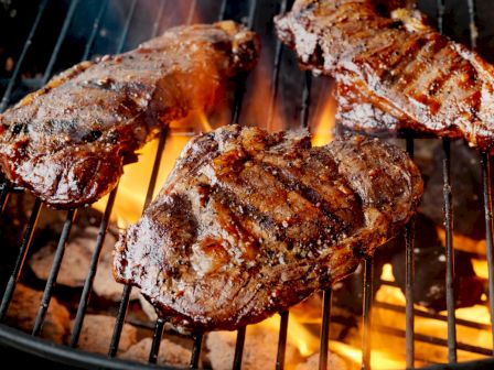Grilled steaks roasting over an open flame on a barbecue grill.