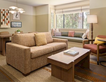 A cozy living room with a beige sofa, coffee table, window blinds, a floor lamp, and soft throw pillows.