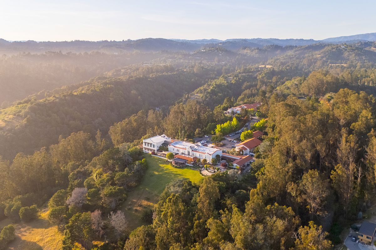 Aerial view of a countryside mansion nestled in green hills and forests at golden hour.