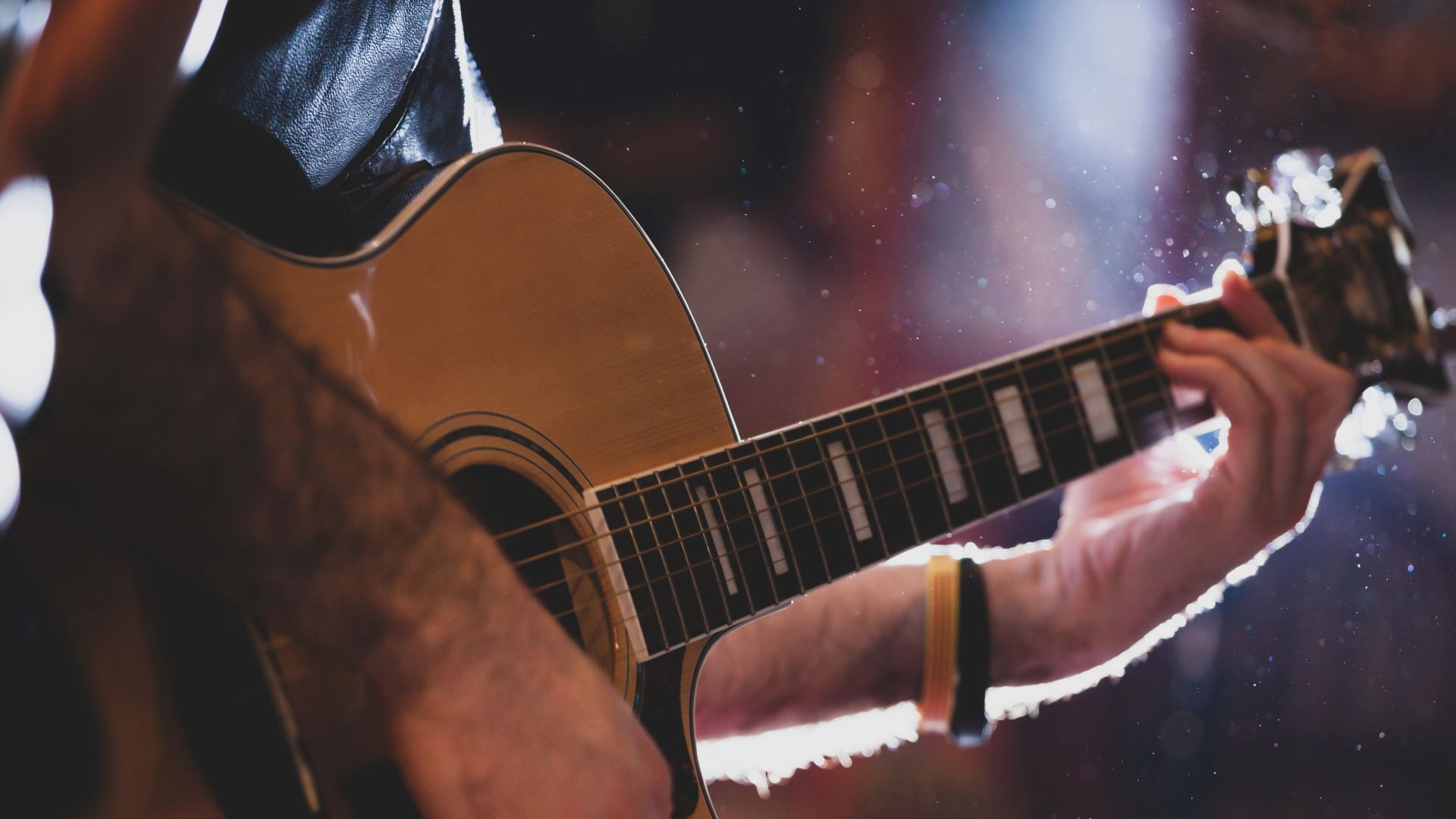 A person playing an acoustic guitar with a focus on the strings and the hands in a softly lit environment.