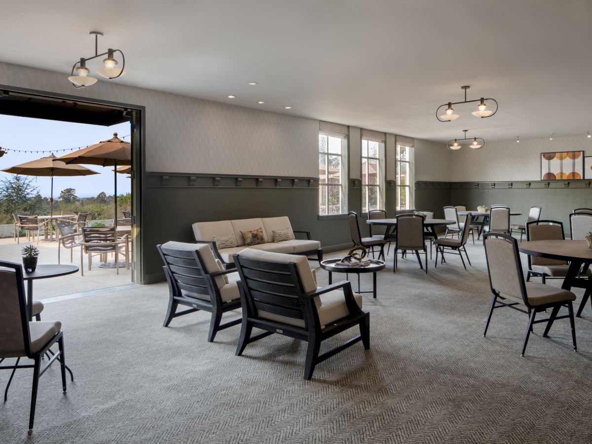 Modern lounge with a sofa, patio doors, tables, dining chairs, hanging lights, and large windowed walls.