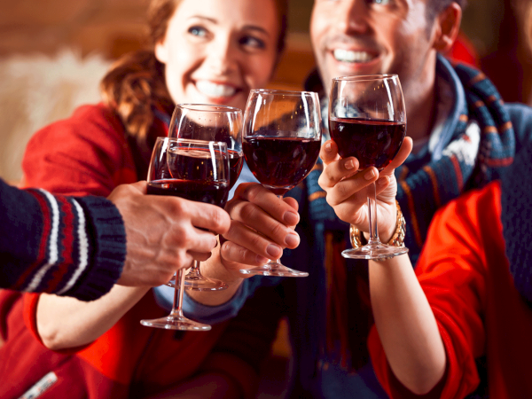 A group of people is raising and clinking glasses of red wine in a cheerful toast. They appear happy and are enjoying their time together.