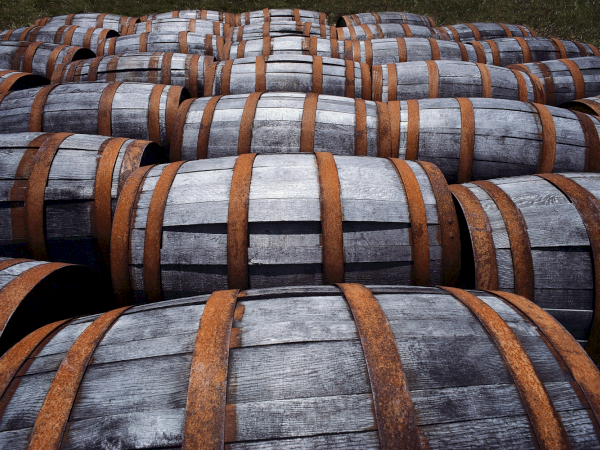 The image shows a collection of wooden barrels with metal bands, arranged closely together, likely used for storing or aging liquids, like wine or whiskey.