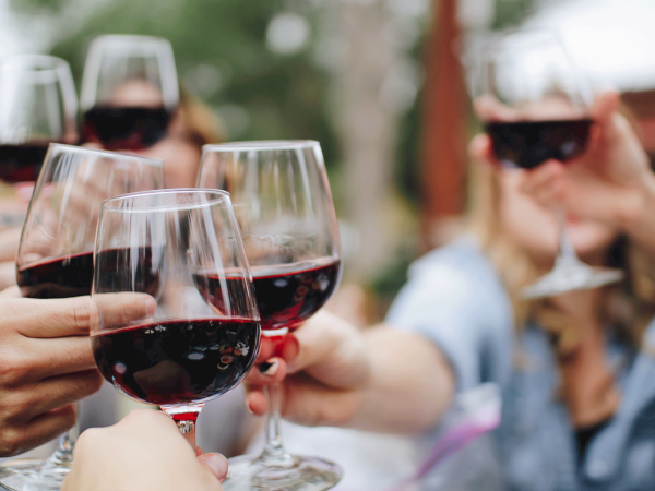 People toasting with glasses of red wine in an outdoor setting.