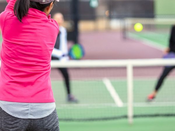 Three people are playing pickleball on an outdoor court, with one player preparing to hit the ball.