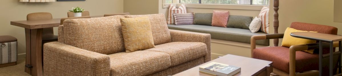 A cozy living room with a beige sofa, coffee table, window blinds, a floor lamp, and soft throw pillows.