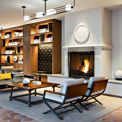 A modern, stylish hair salon with large windows, warm lighting, and sleek black chairs; mirrors line the wall, creating a chic, inviting workspace.
