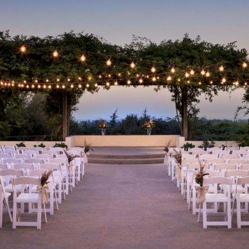 A tropical beach wedding setup with rows of white chairs facing a decorated arch and a calm, turquoise sea in the background.