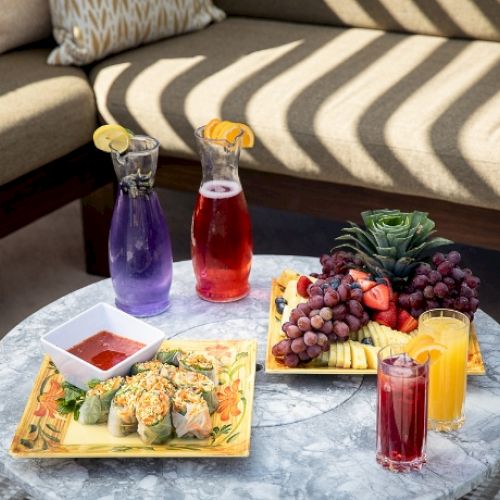 Appetizing breakfast or brunch spread on a table with waffles, fruit, pastries, and drinks, set beside a cozy striped sofa.