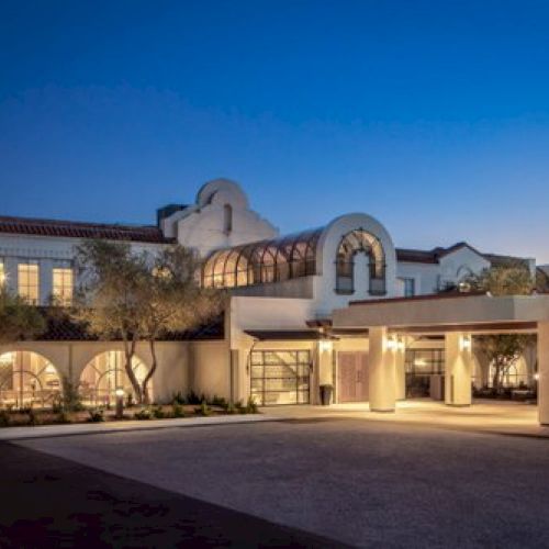 A modern suburban house with stone and stucco facade, a tiled roof, and a gated driveway under a clear blue sky.