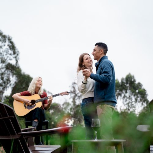 Outdoor music: a guitarist plays while a smiling couple holds hands and dances in a garden.