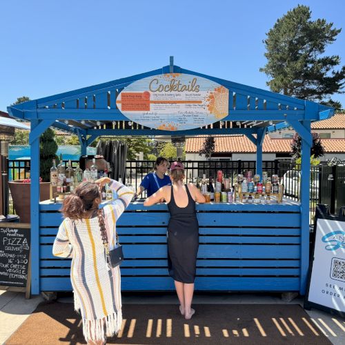 A small group of people pose in front of a blue sign and storefront at an outdoor market or fair.