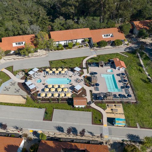Aerial view of a residential complex with a central pool, playgrounds, and surrounding greenery, sunny day, neighborhood layout.