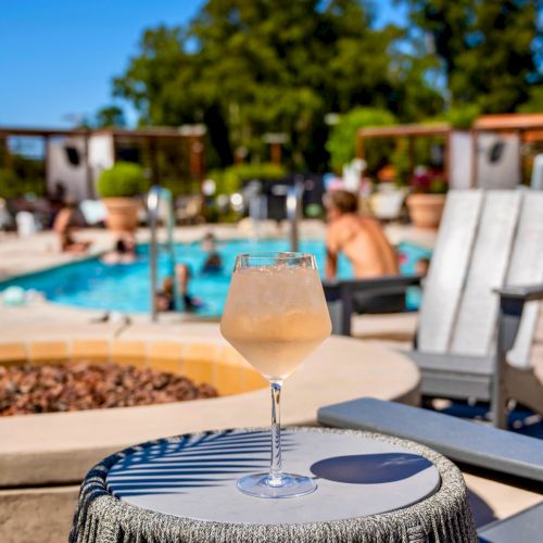 A sunny poolside scene with lounge chairs, umbrellas, a thatched-roof cabana, and people relaxing by a turquoise pool under blue skies.