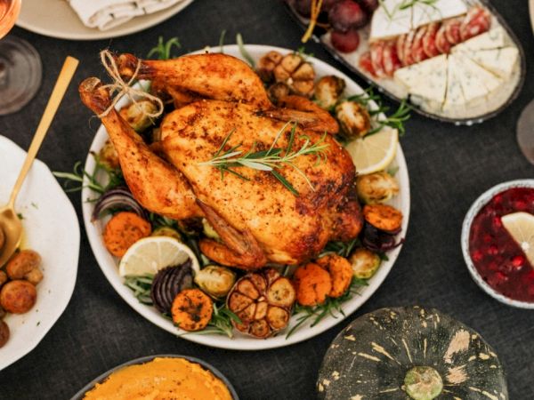 A platter of roasted chicken with lemon, herbs, roasted veggies, and wine on a dinner table.