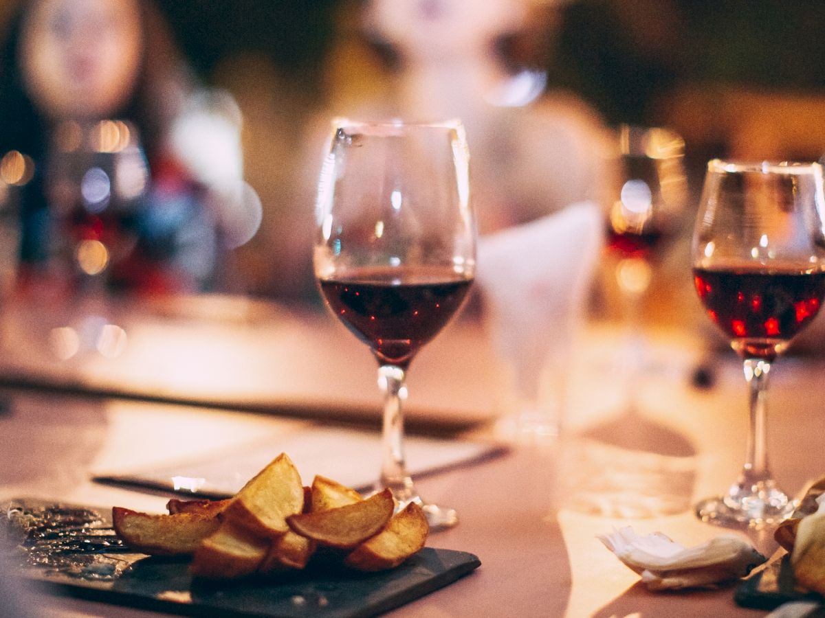 A social dinner scene with wine glasses, plated appetizers, warm lighting, and blurred guests in the background.