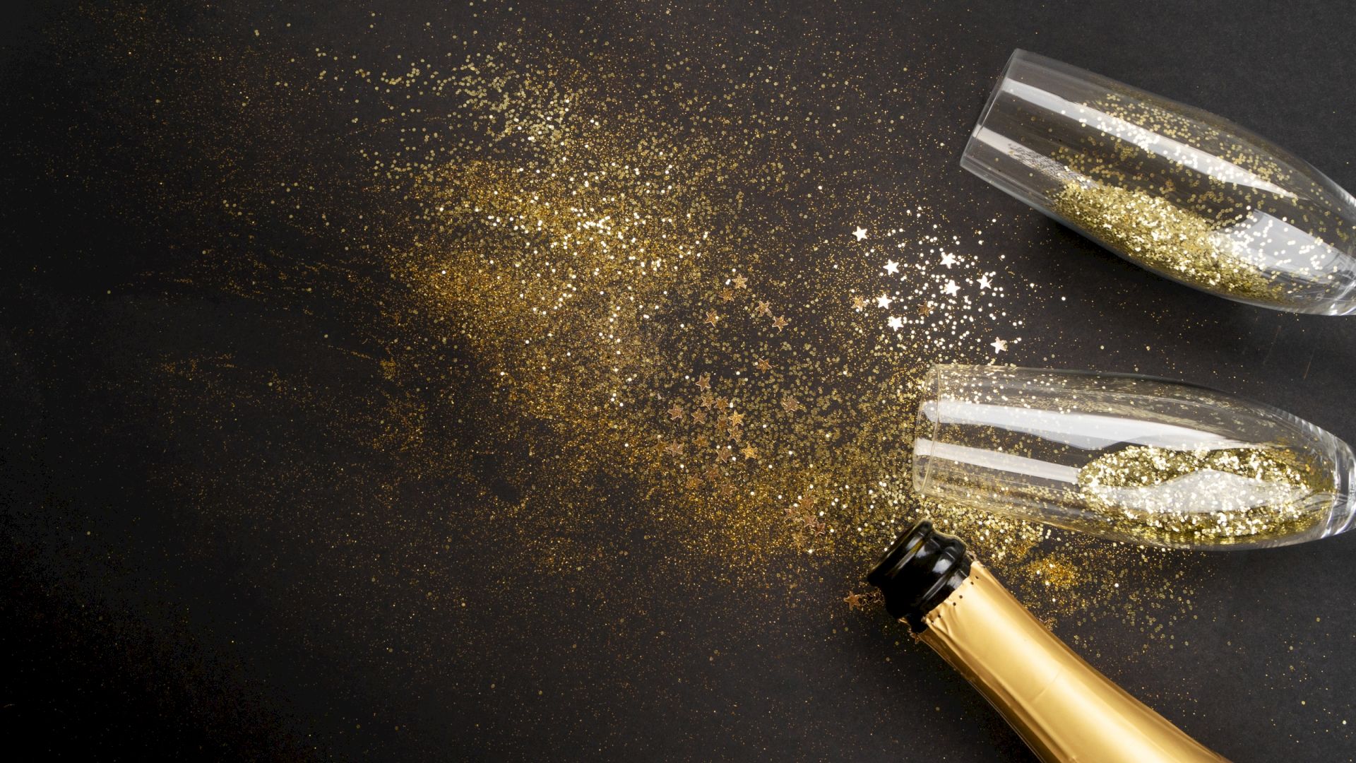 A champagne bottle and two glasses lie on a black surface with scattered gold glitter and star confetti.