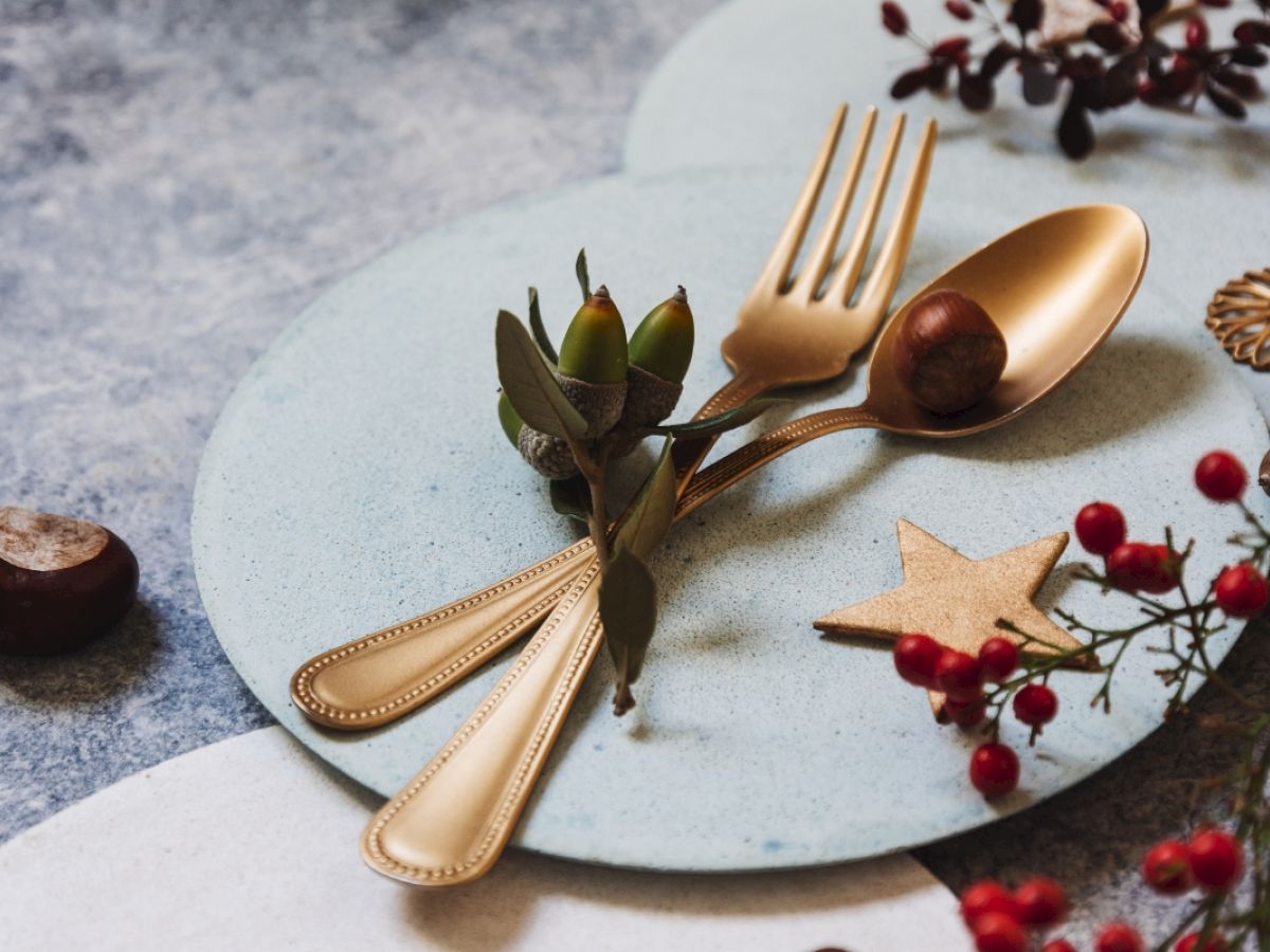 The image shows a decorative arrangement with a fork, spoon, leaves, berries, and a star on a plate. A rustic and festive setting.
