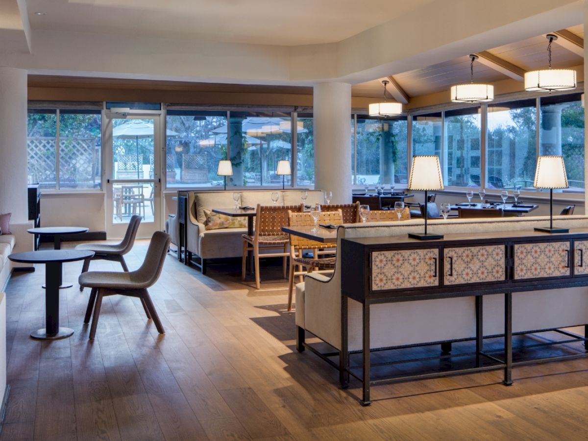A modern restaurant interior with wooden floors, tables, chairs, and ceiling lights, offering a cozy ambiance.