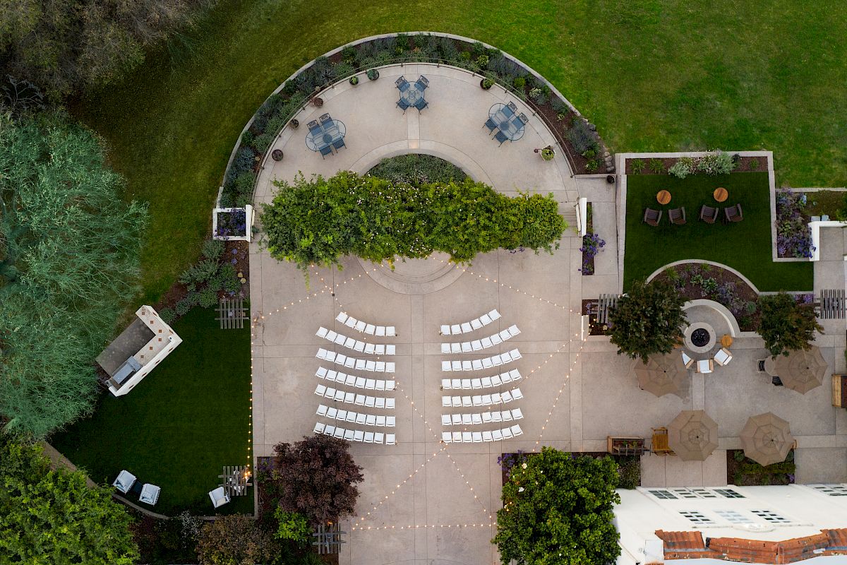 An aerial view of a patio setup for an event, with chairs, tables, greenery, and string lights creating an elegant outdoor atmosphere.
