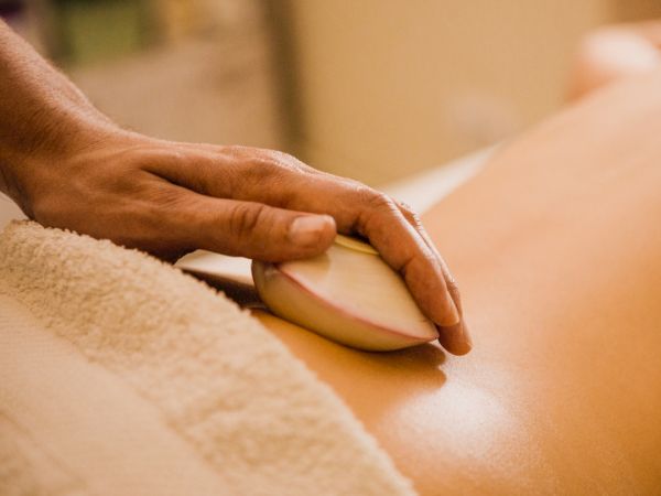 A hand is holding a hot stone over a person's back, covered with a towel, likely during a spa or massage therapy session.