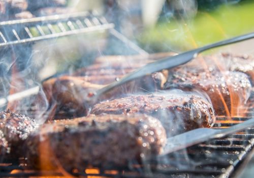 Smoked barbecue grilling: sausages and meat roast on a hot grill, with thick steam and charred edges.