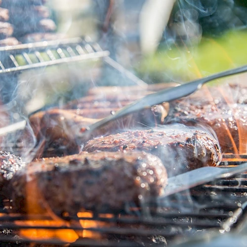 Smoked barbecue grilling: sausages and meat roast on a hot grill, with thick steam and charred edges.