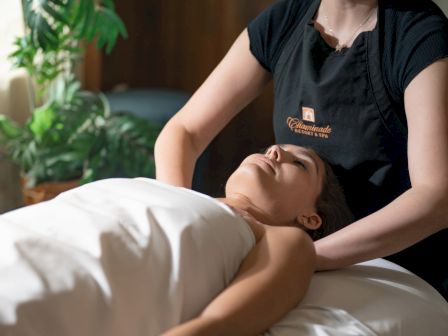 A massage therapist gives a facial massage to a client lying on a bed in a spa.