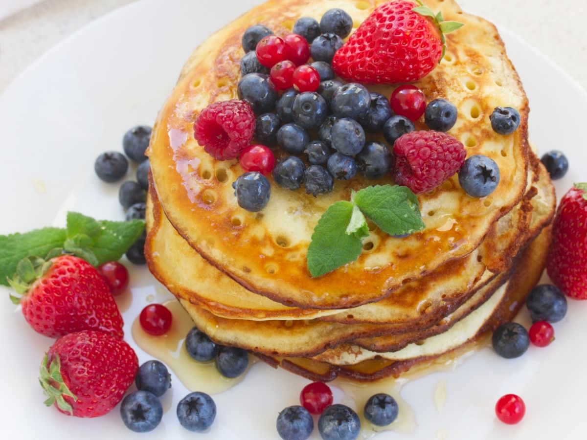 Stack of pancakes topped with strawberries, blueberries, raspberries, and mint on a white plate.
