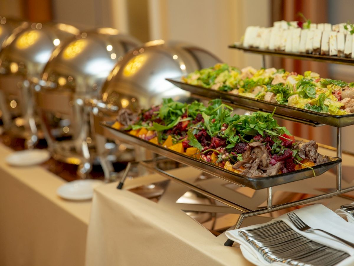 A catering buffet with chafing trays of salads and sides on display at a banquet table.