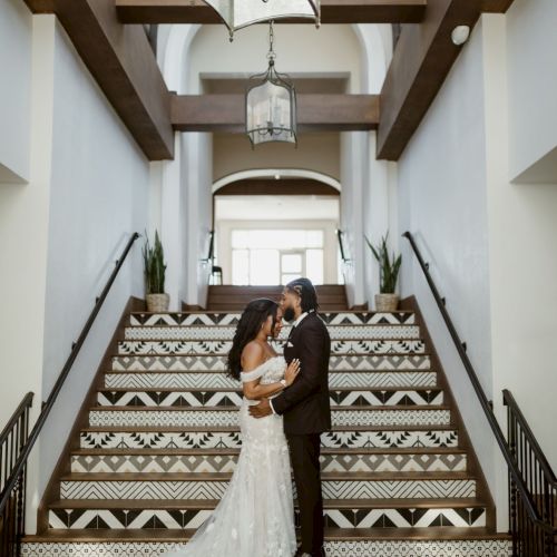 A bride and groom embrace on a decorative staircase inside a bright wedding venue.