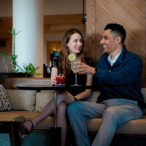 Two friends relaxing at a cozy bar, sharing drinks and smiles while chatting warmly.